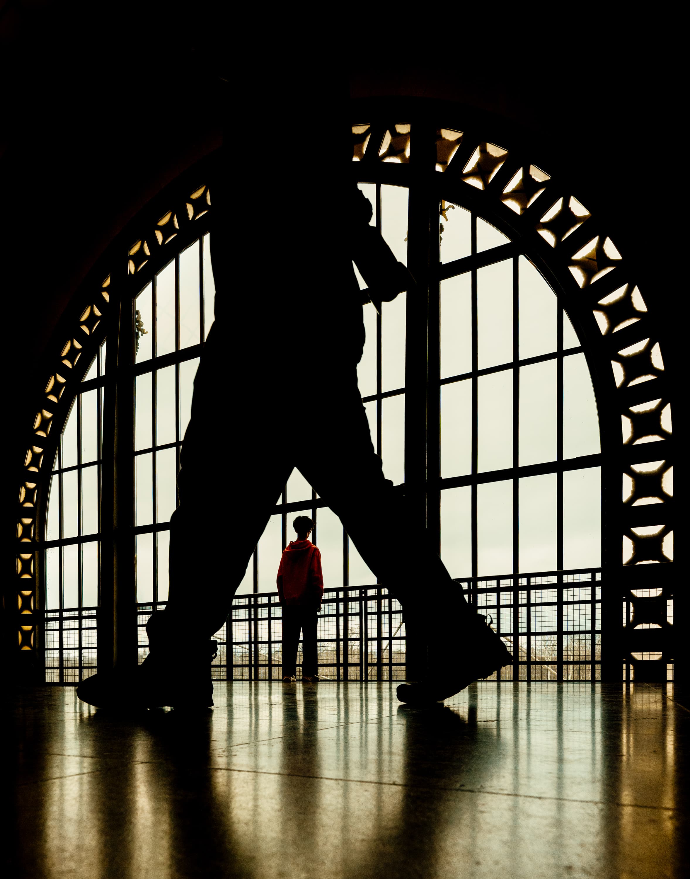 Dramatic silhouette framing a child in red jacket at Musée d'Orsay clock window, Paris — street photography