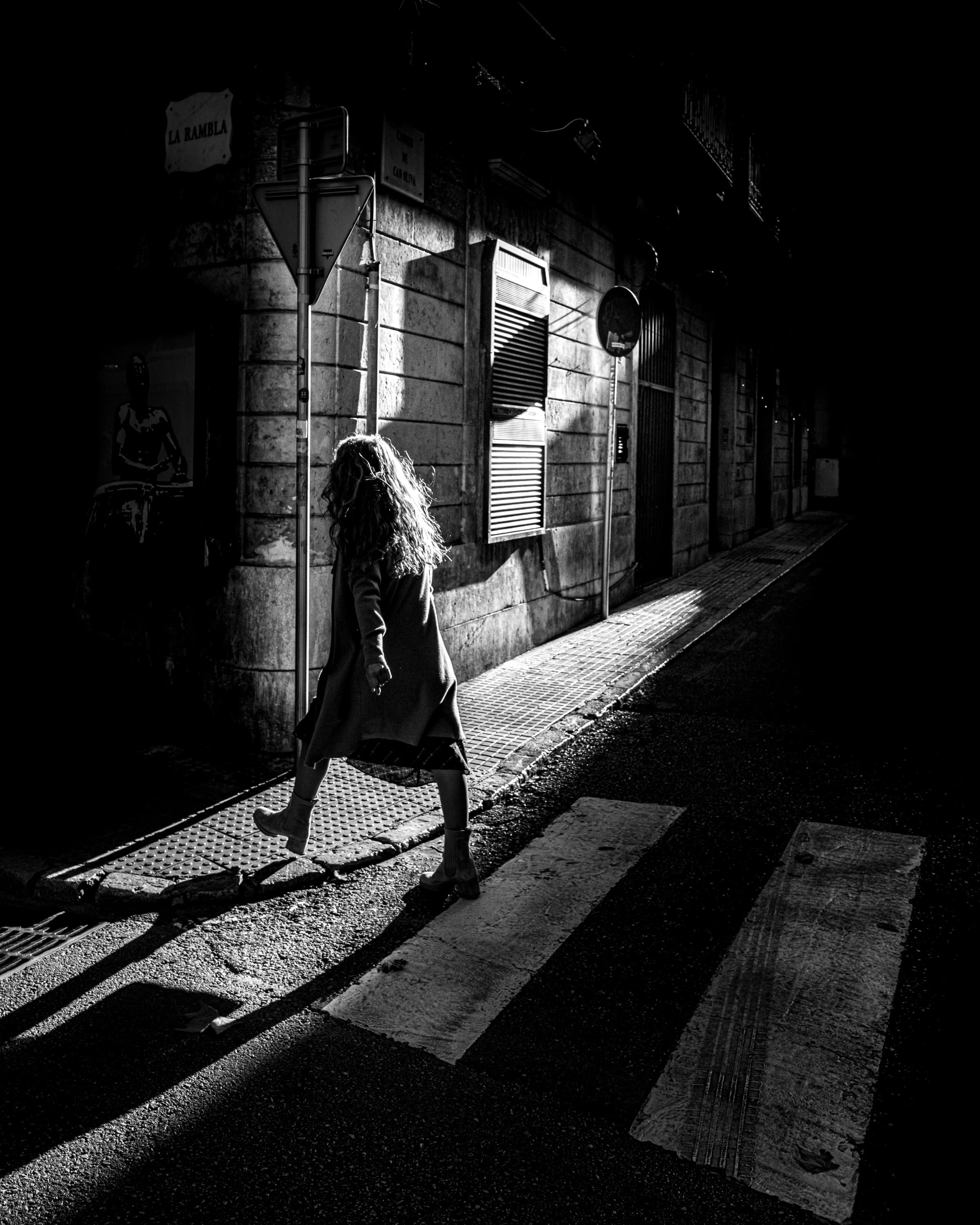 Woman walking through backlit alley near La Rambla at night, Palma de Mallorca — black and white street photography