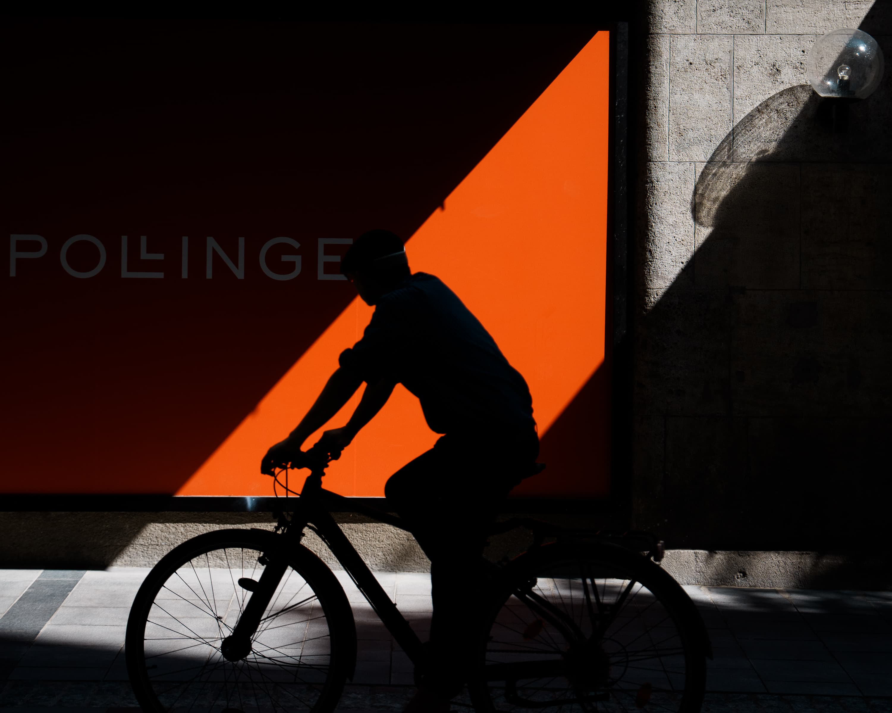 Cyclist silhouette passing orange storefront with diagonal shadow, Palma de Mallorca — color street photography