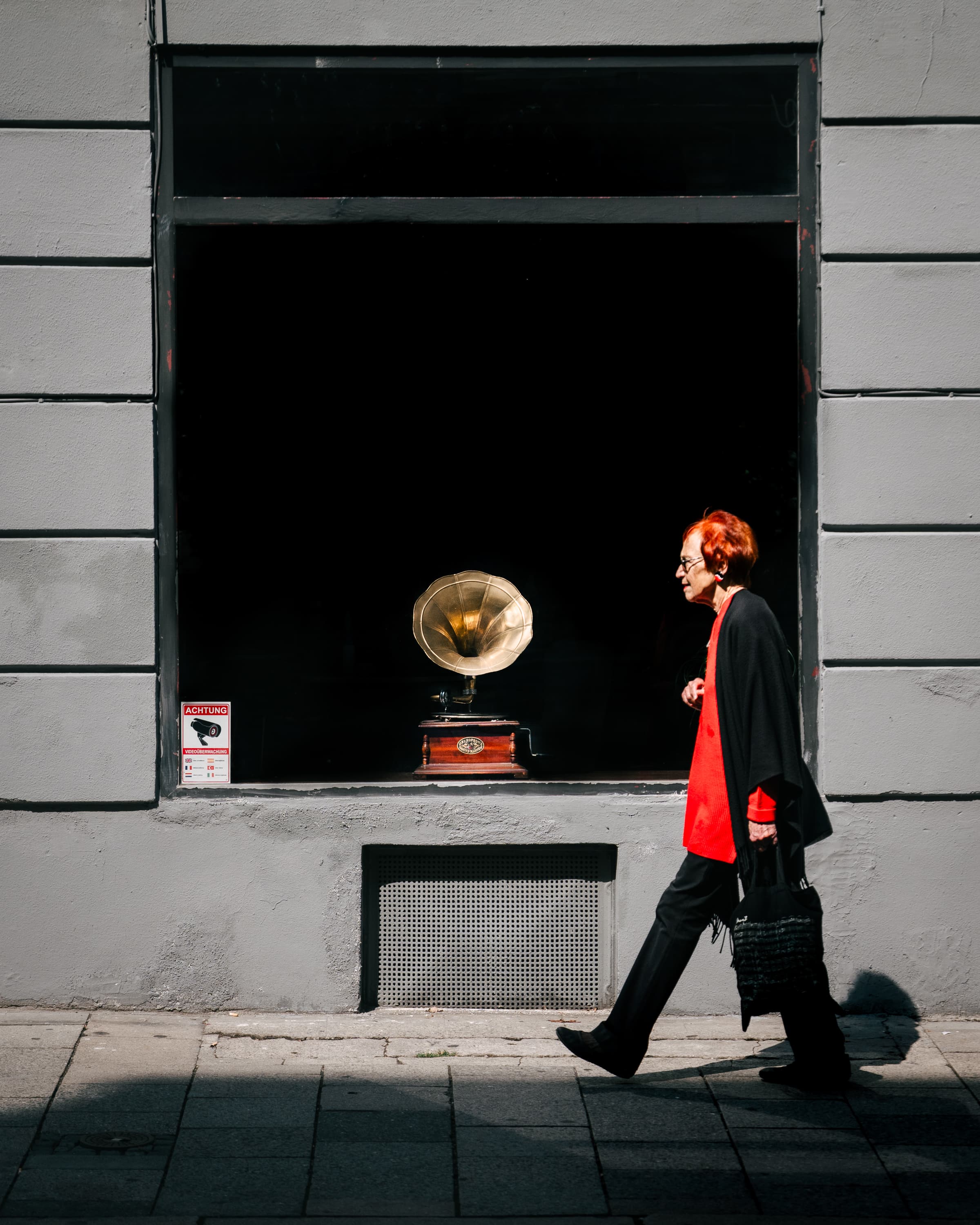 Elegant woman in red walking past antique gramophone in shop window, Berlin — color street photography