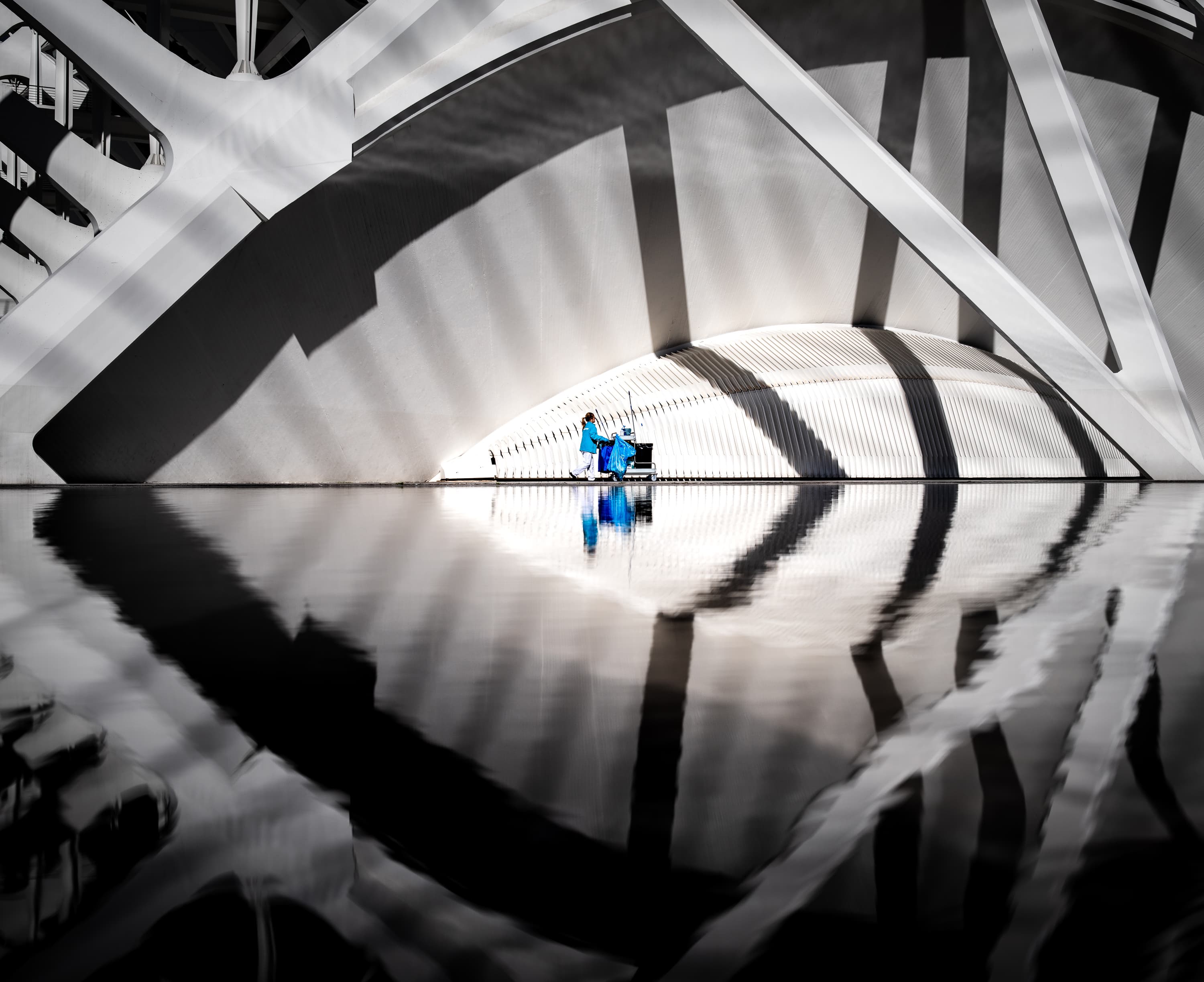 Cleaning worker in blue beneath Calatrava bridge with perfect water reflection at Ciudad de las Artes, Valencia — selective color