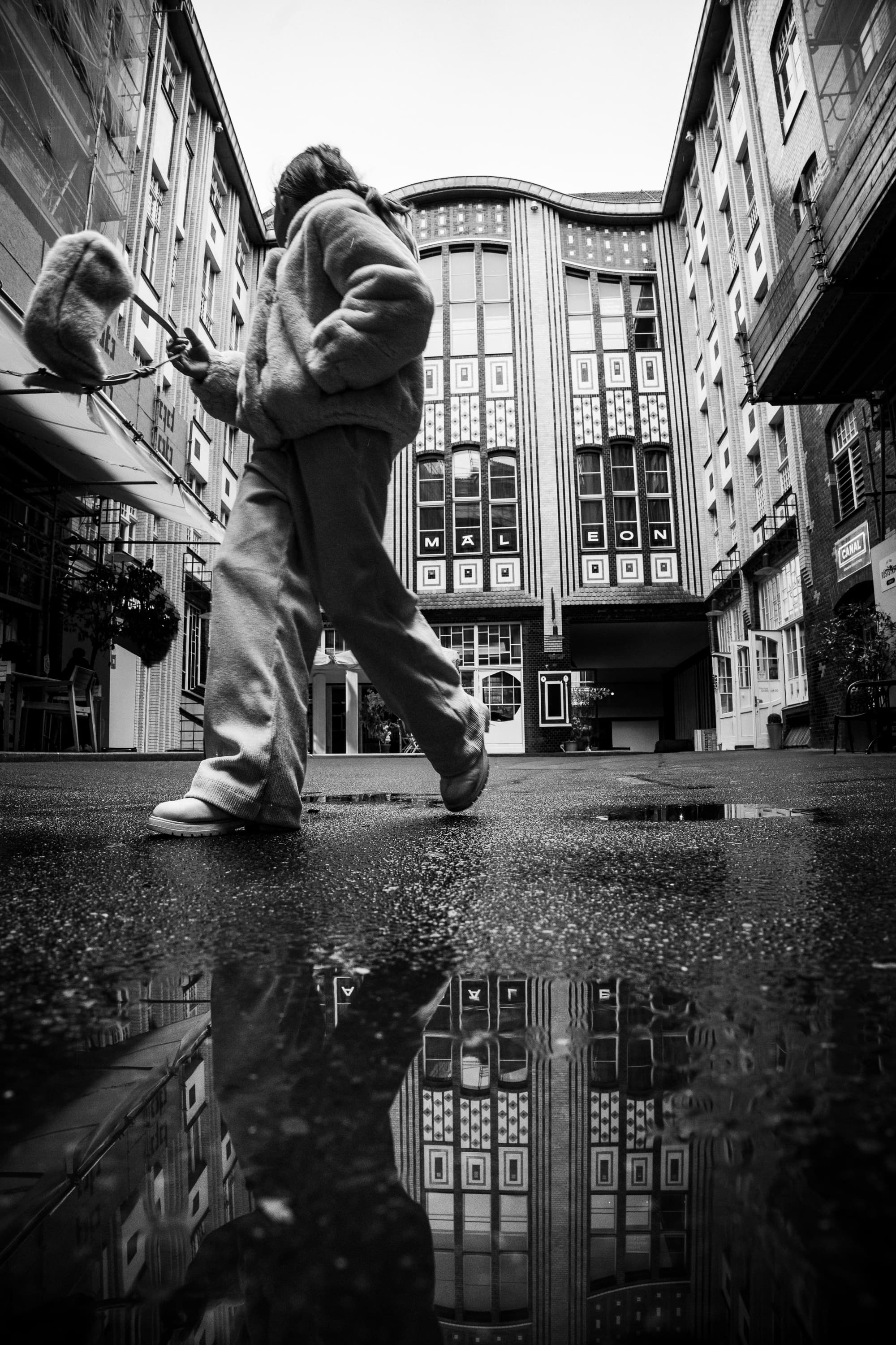 Person walking past Hackesche Höfe in Berlin, low angle with puddle reflection — black and white street photography