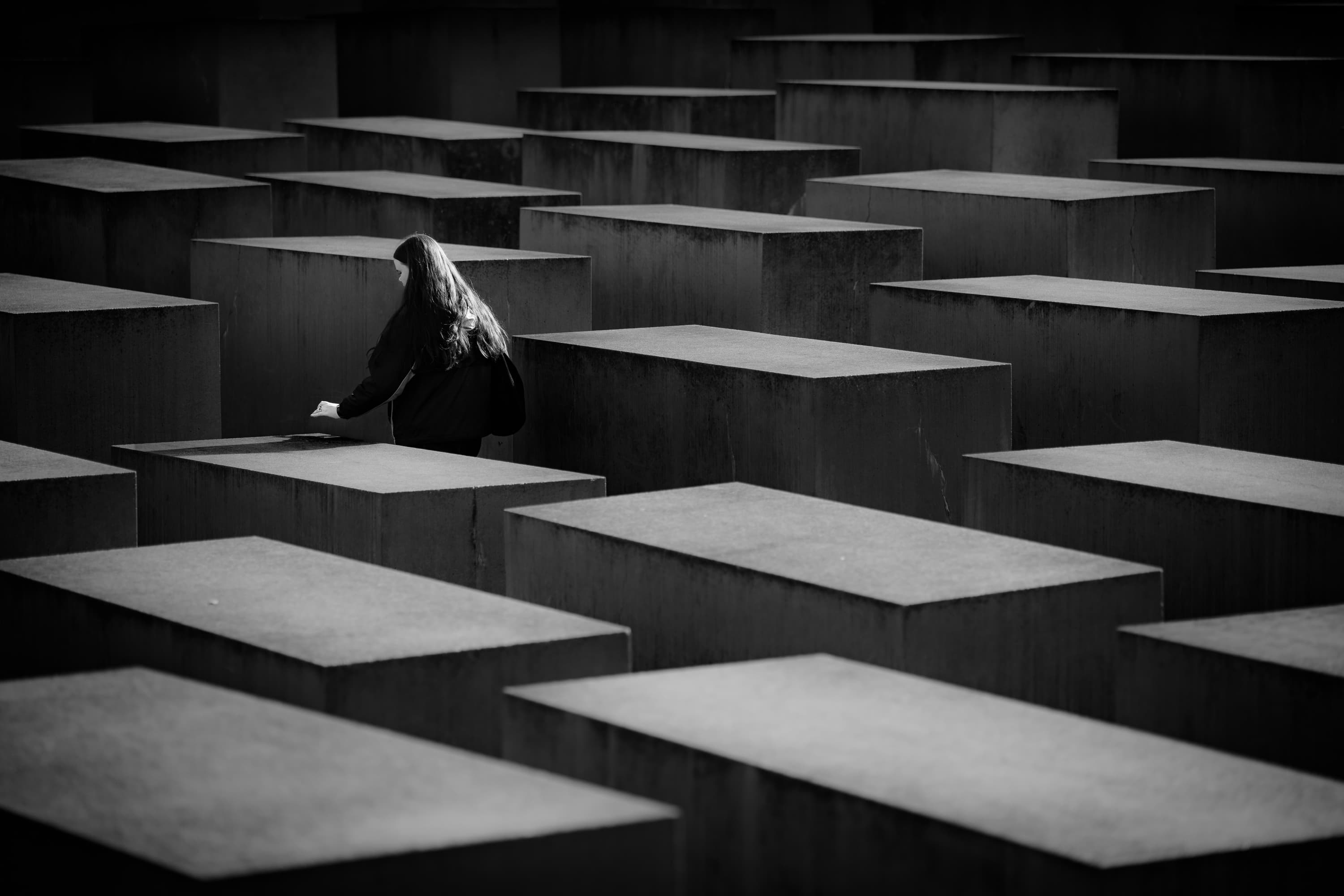 Woman walking between concrete stelae at the Holocaust Memorial, Berlin — black and white documentary photography