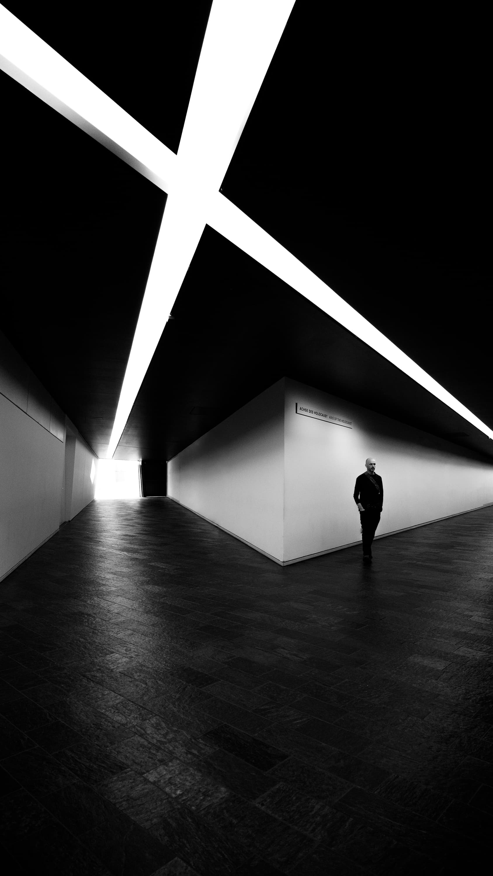 Solitary figure in the void of the Jewish Museum Berlin, Libeskind architecture with dramatic light slashes — black and white