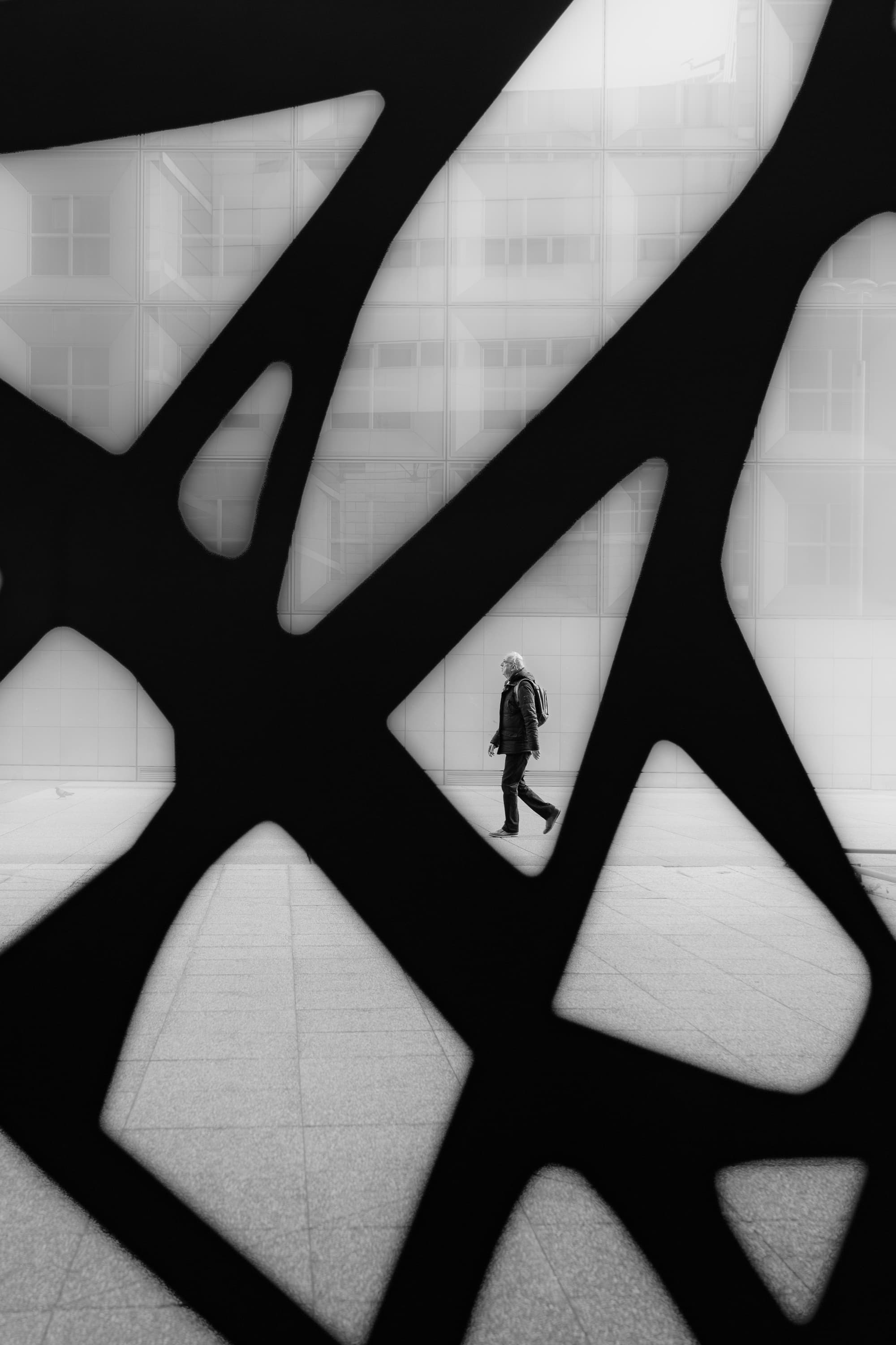 Lone figure framed by abstract sculpture silhouette at La Défense, Paris — black and white urban photography