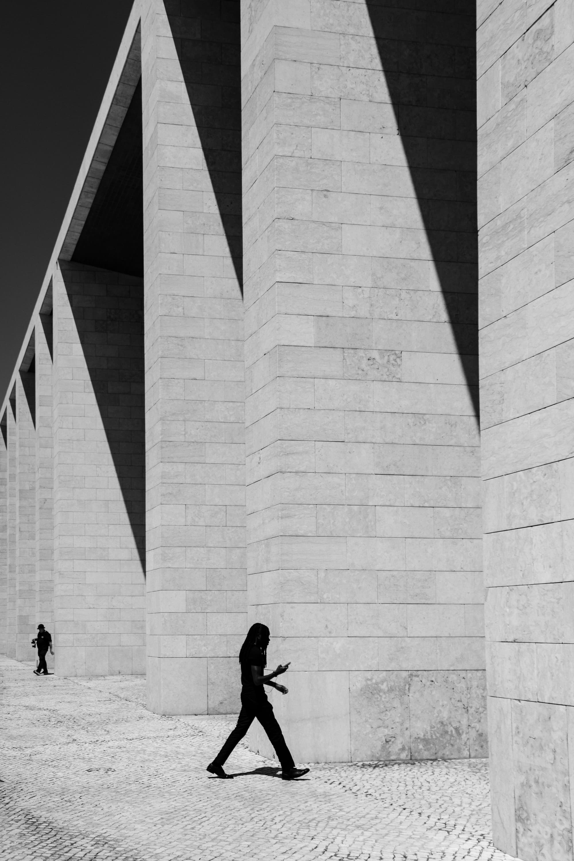 Woman walking past monumental stone columns with geometric shadows — black and white architectural street photography