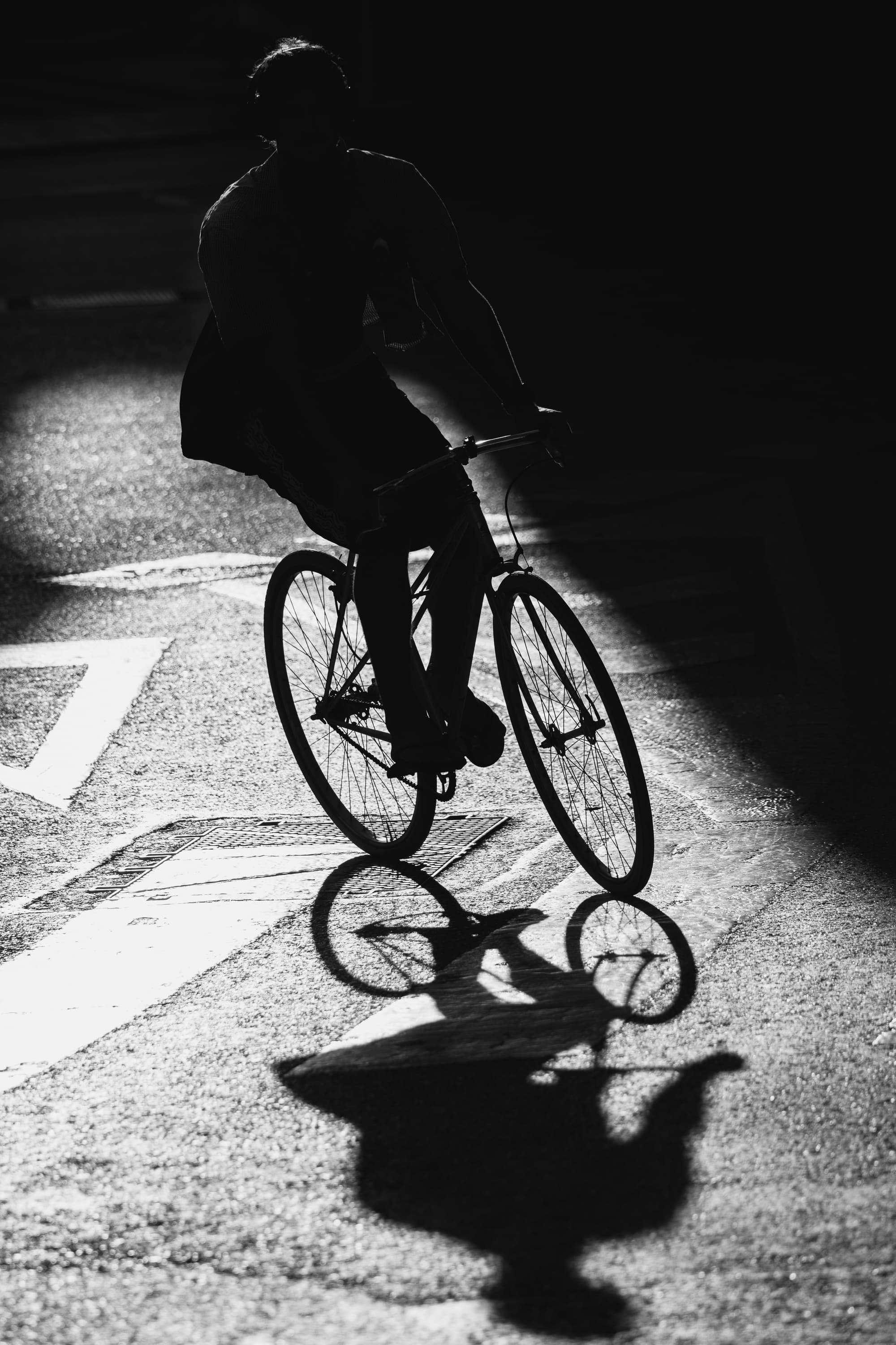 Cyclist silhouette in dramatic backlight with shadow on asphalt — black and white street photography