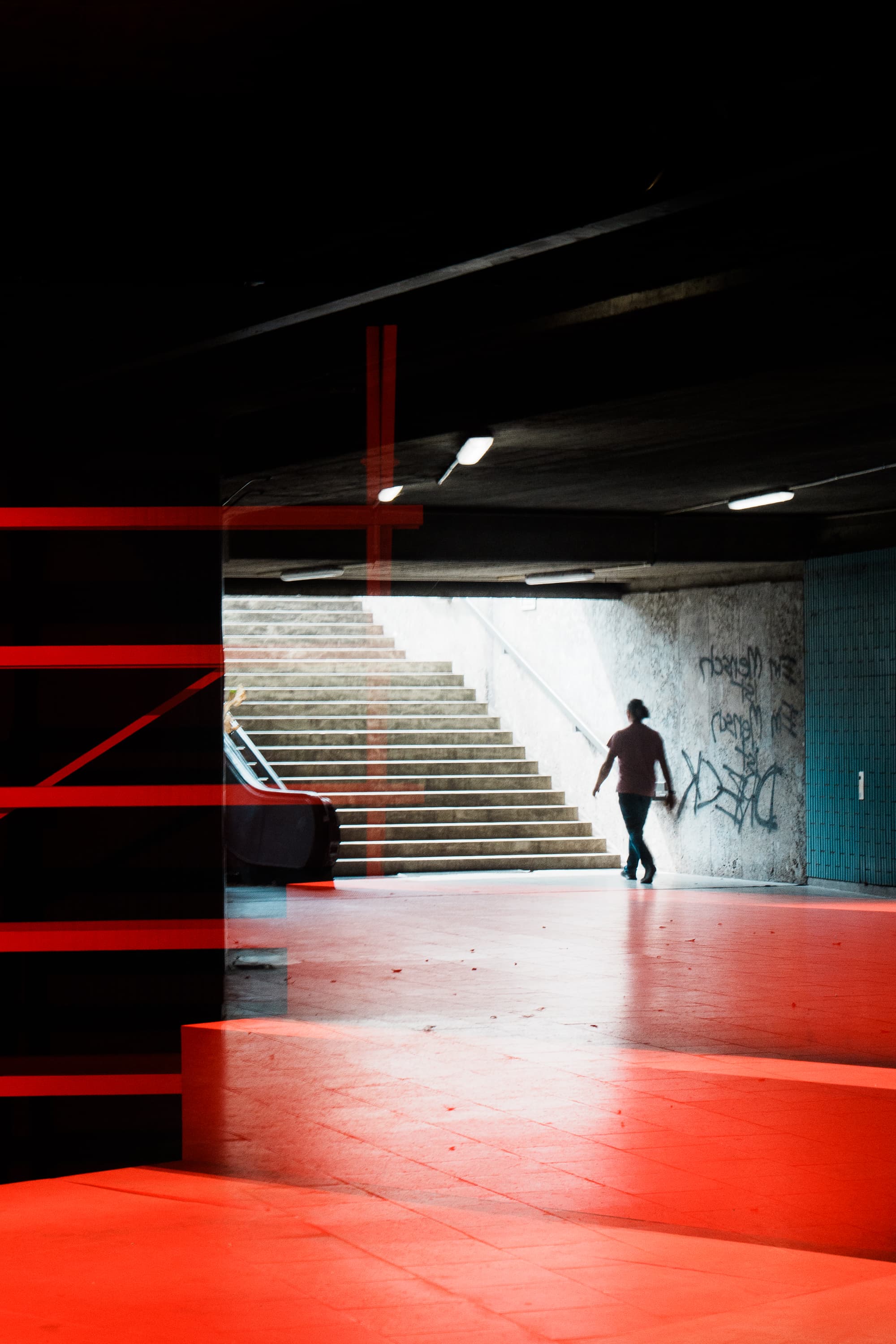 Person ascending stairs from red-floored urban underpass with graffiti into daylight — color street photography Berlin